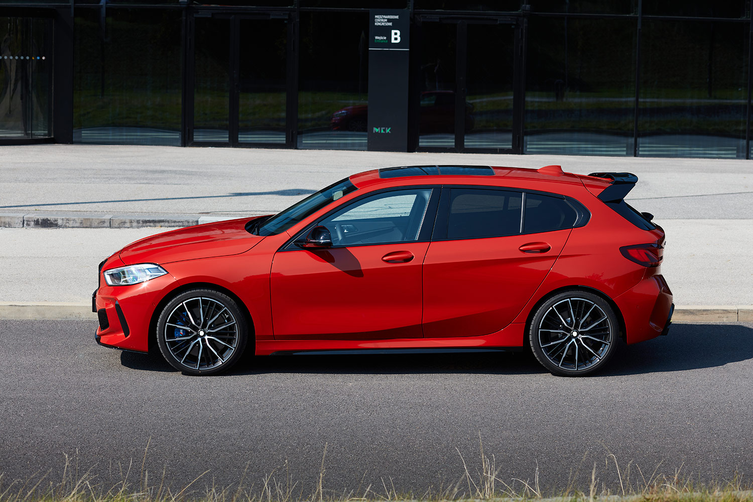 Red hatchback parked on a forecourt in front of a glass building