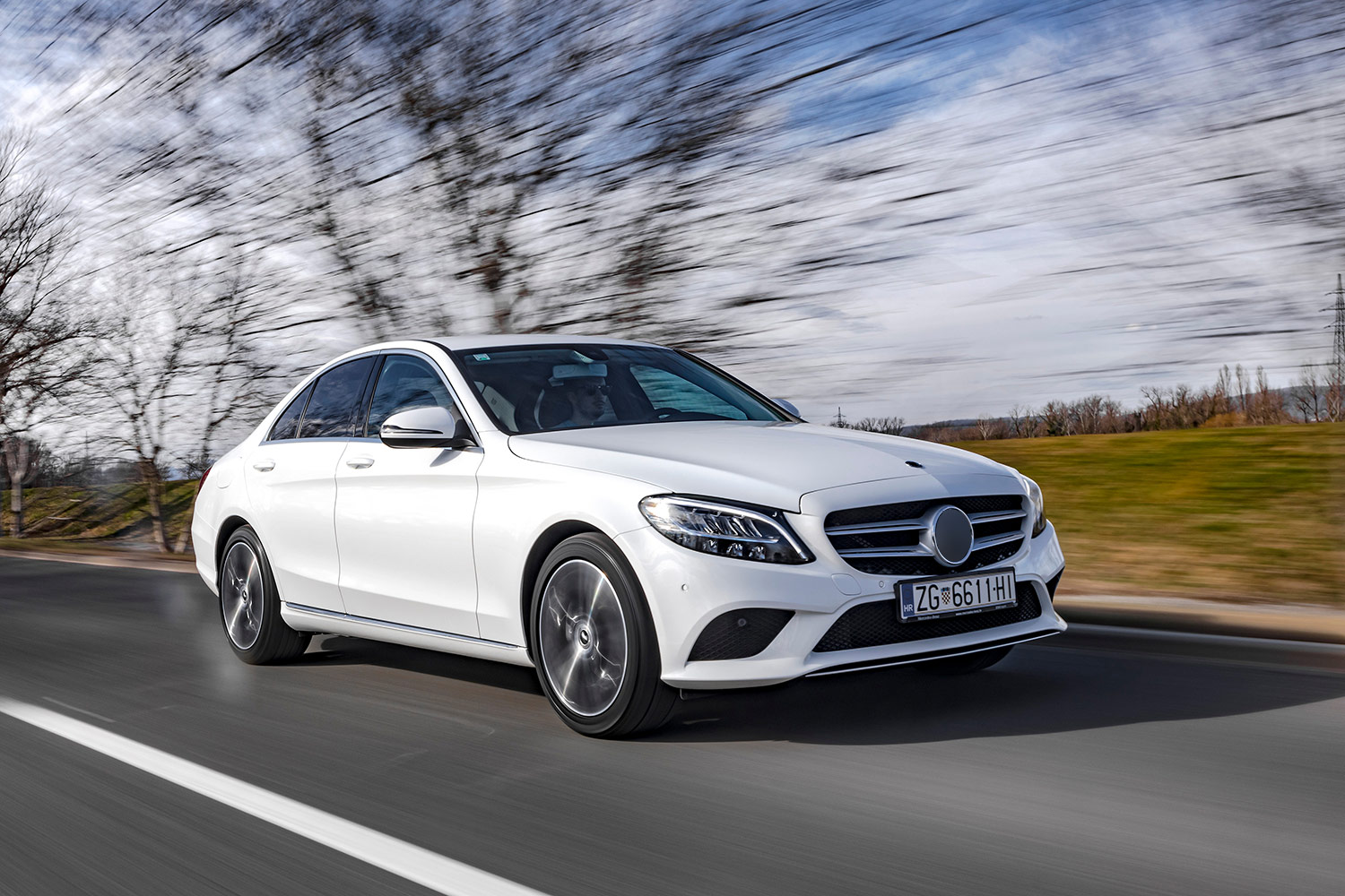 White sedan photographed in motion on a road, background blurred